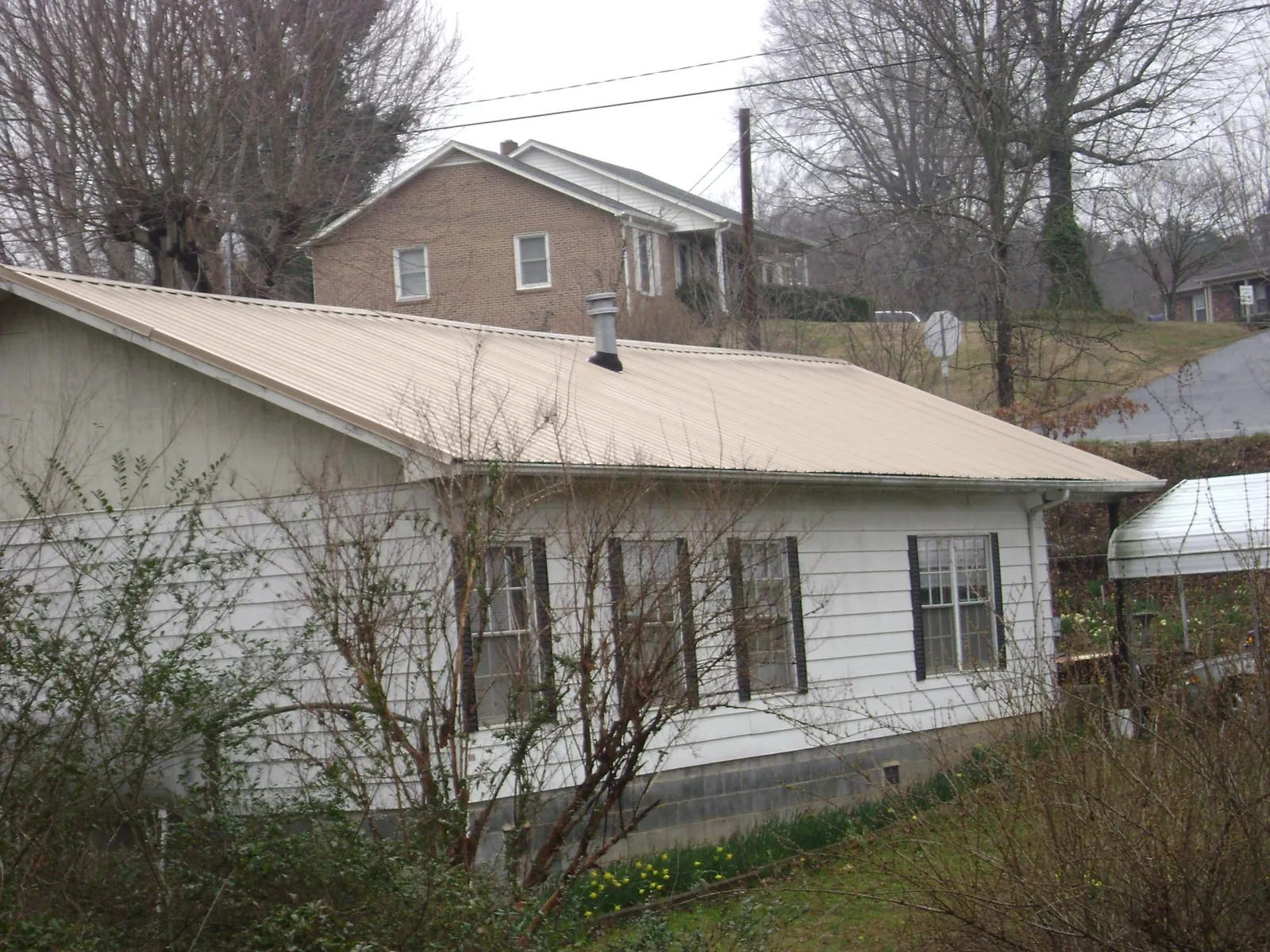Tan metal roof on a white sided house set into a hillside — Commercial Roofing by Roofing Brothers in Clarksdale