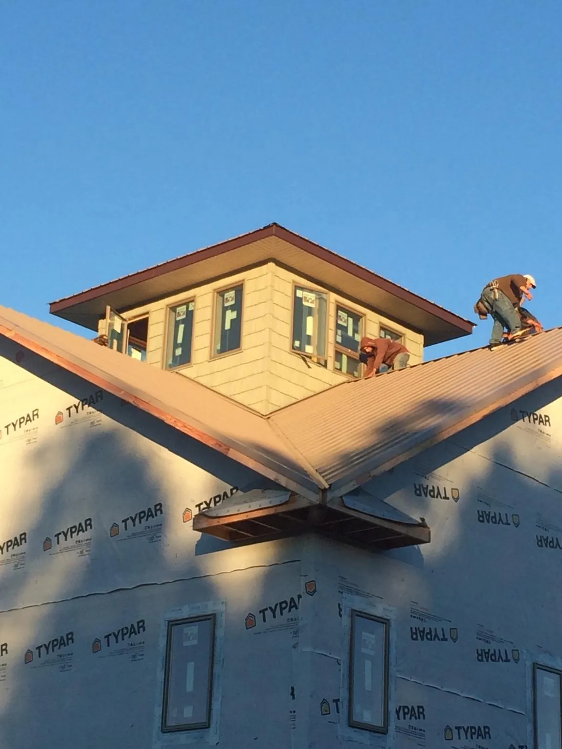 Roofers working around a rooftop cupola on a new metal roof at sunset — Roof Waterproofing in Clarksdale by Roofing Brothers